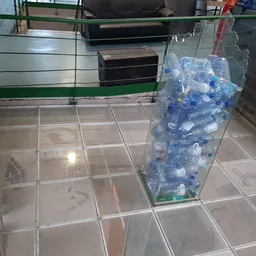 Winkelvloer met tegel, grote bak vol plastic flessen voor recycling, en zwarte dozen op achtergrond