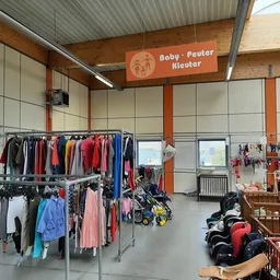Winkelinterieur met rekken babykleding, kinderwagen en speelgoed onder oranje-wit signage