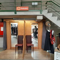 Winkelinterieur met houten deur, bruine stoelen, kleding op hangers en stellingen onder trap