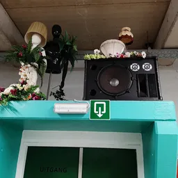 Turquoise winkelingang met groene deur en decoratieve items op het dak, waaronder speakers en kunstbloemen
