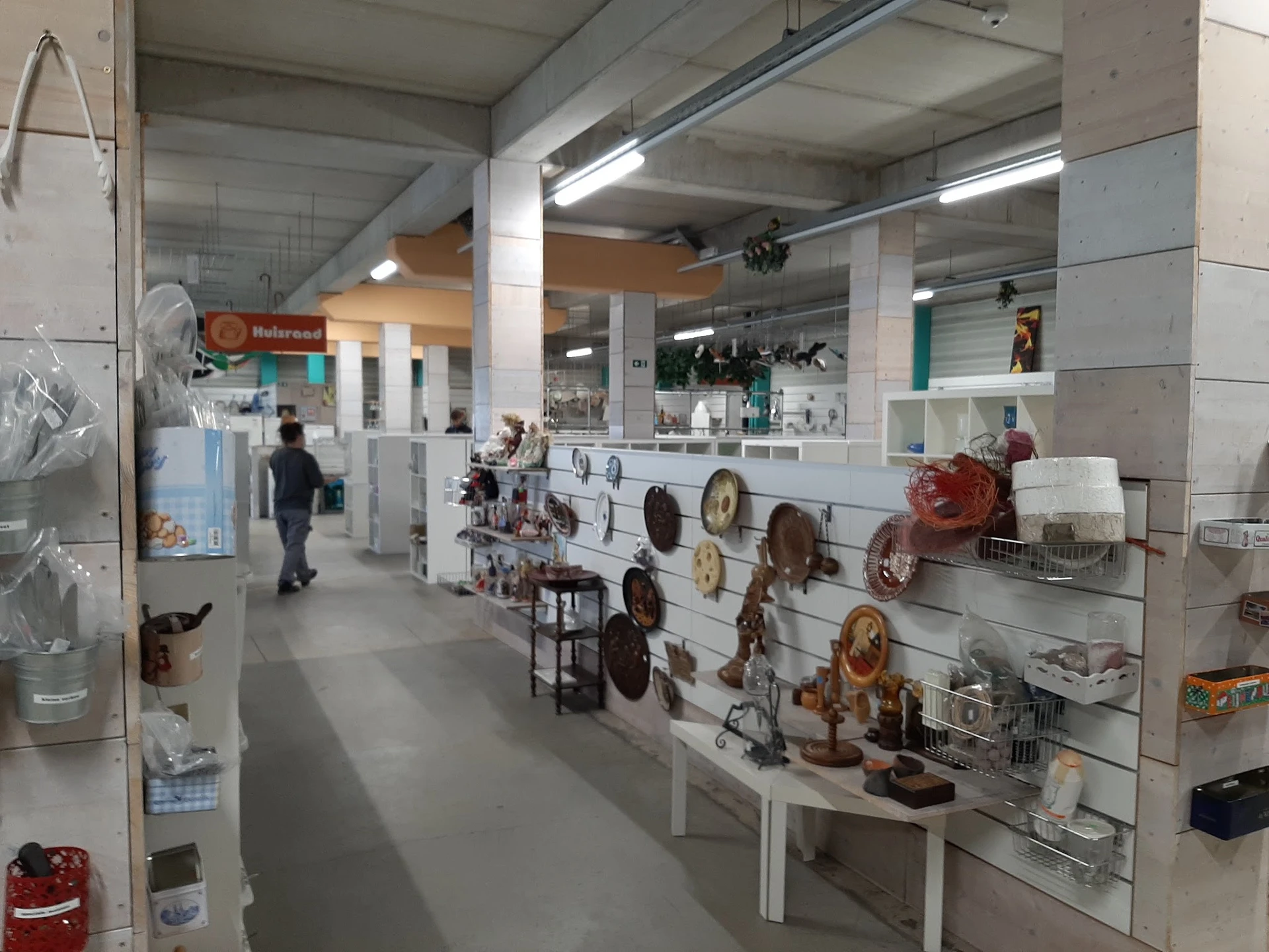Winkelruimte met display aan rechtermuur met kookgerei en potten, stellingen met artikelen, betaalbalies op achtergrond