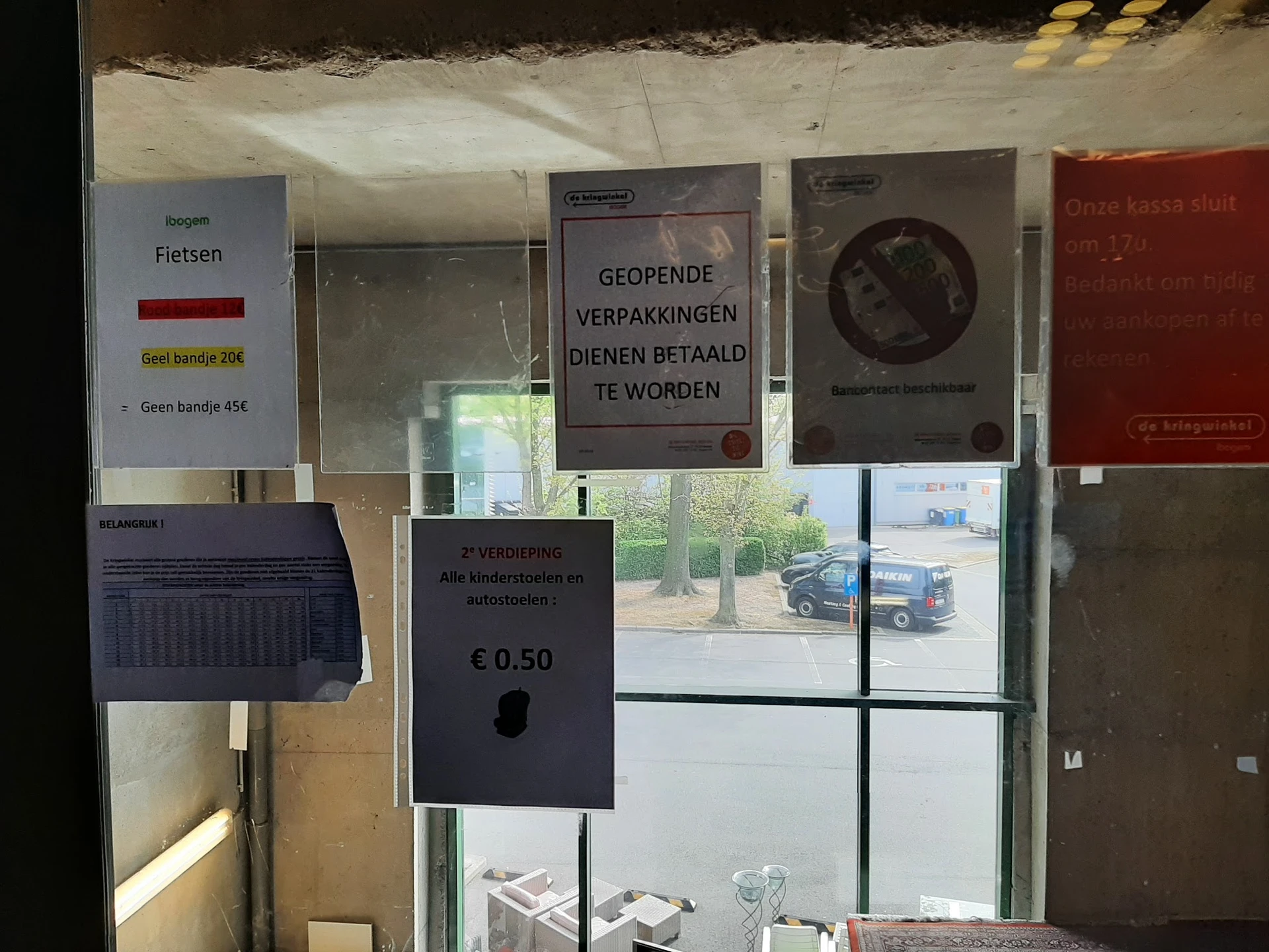Winkelraam met informatieborden, parkeerautomaat en uitzicht op parkeerterrein