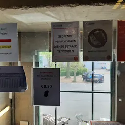 Winkelraam met informatieborden, parkeerautomaat en uitzicht op parkeerterrein