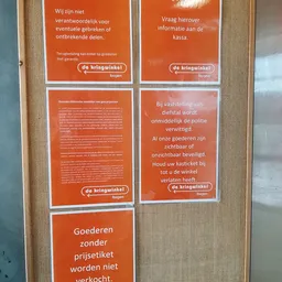 Informatieposters van de Kringwinkel met huisregels en richtlijnen op oranje achtergrond