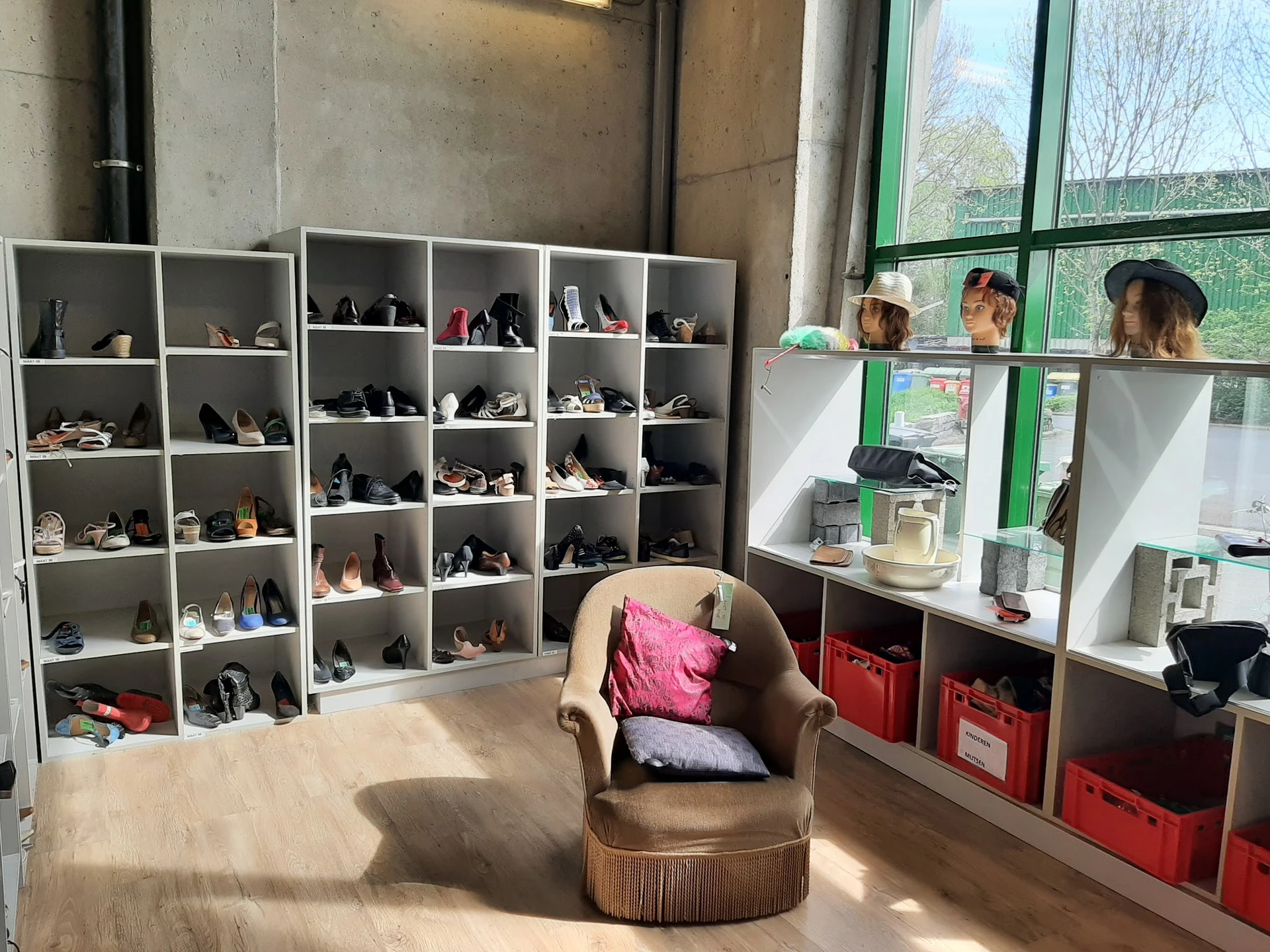 Winkelinterieur met schoenensorteerkasten, een bruine fauteuil en rood opbergmeubilair