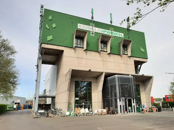 Voorkant van een groot modern kringloopwinkelgebouw met groene bovenbouw en beige onderbouw, naam zichtbaar op gevel