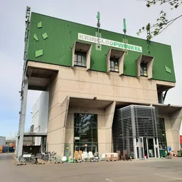 Voorkant van een groot modern kringloopwinkelgebouw met groene bovenbouw en beige onderbouw, naam zichtbaar op gevel