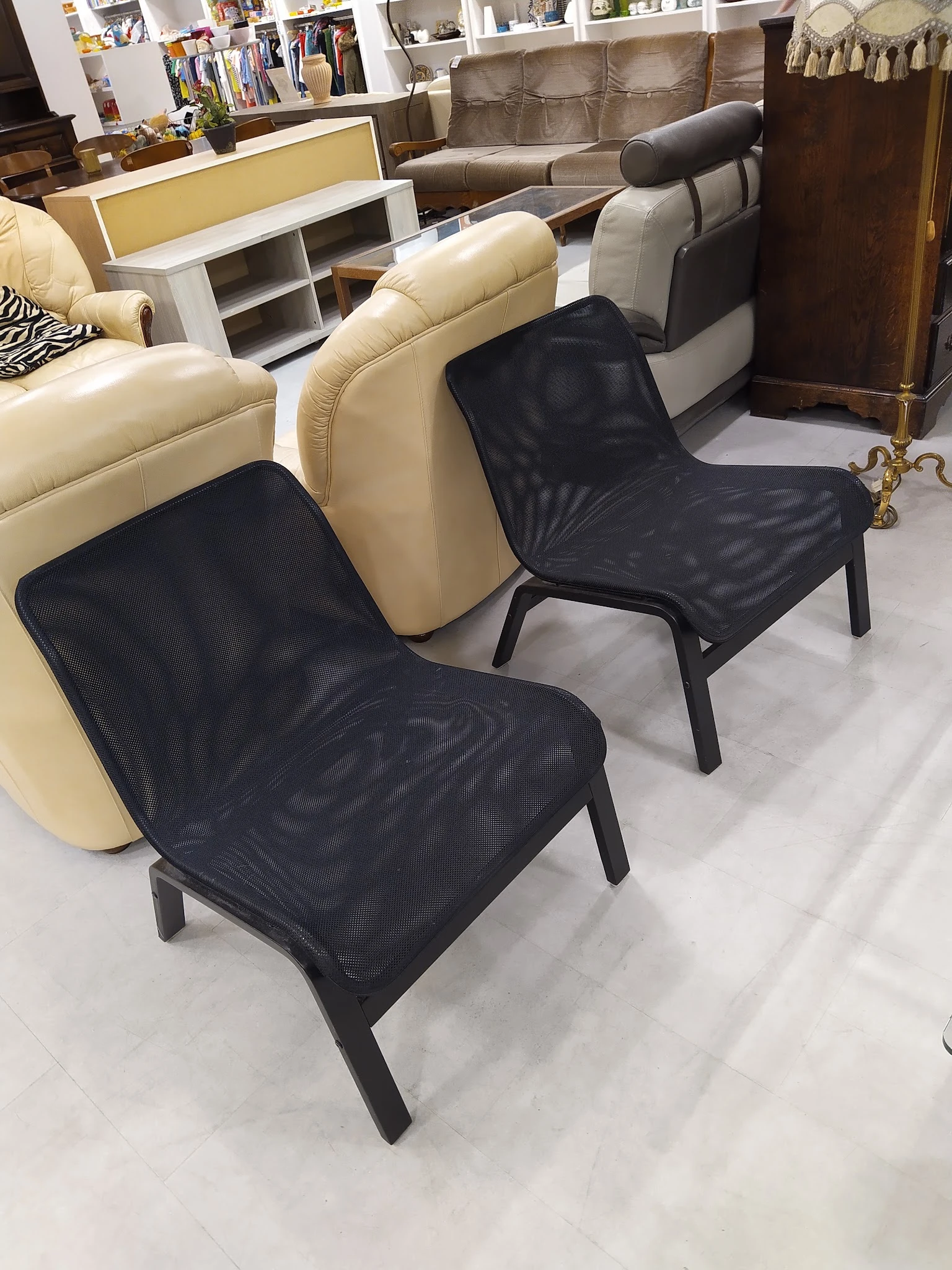 Twee zwarte modern design stoelen met mesh zitting en zwart stalen frame naast crèmekleurige bank