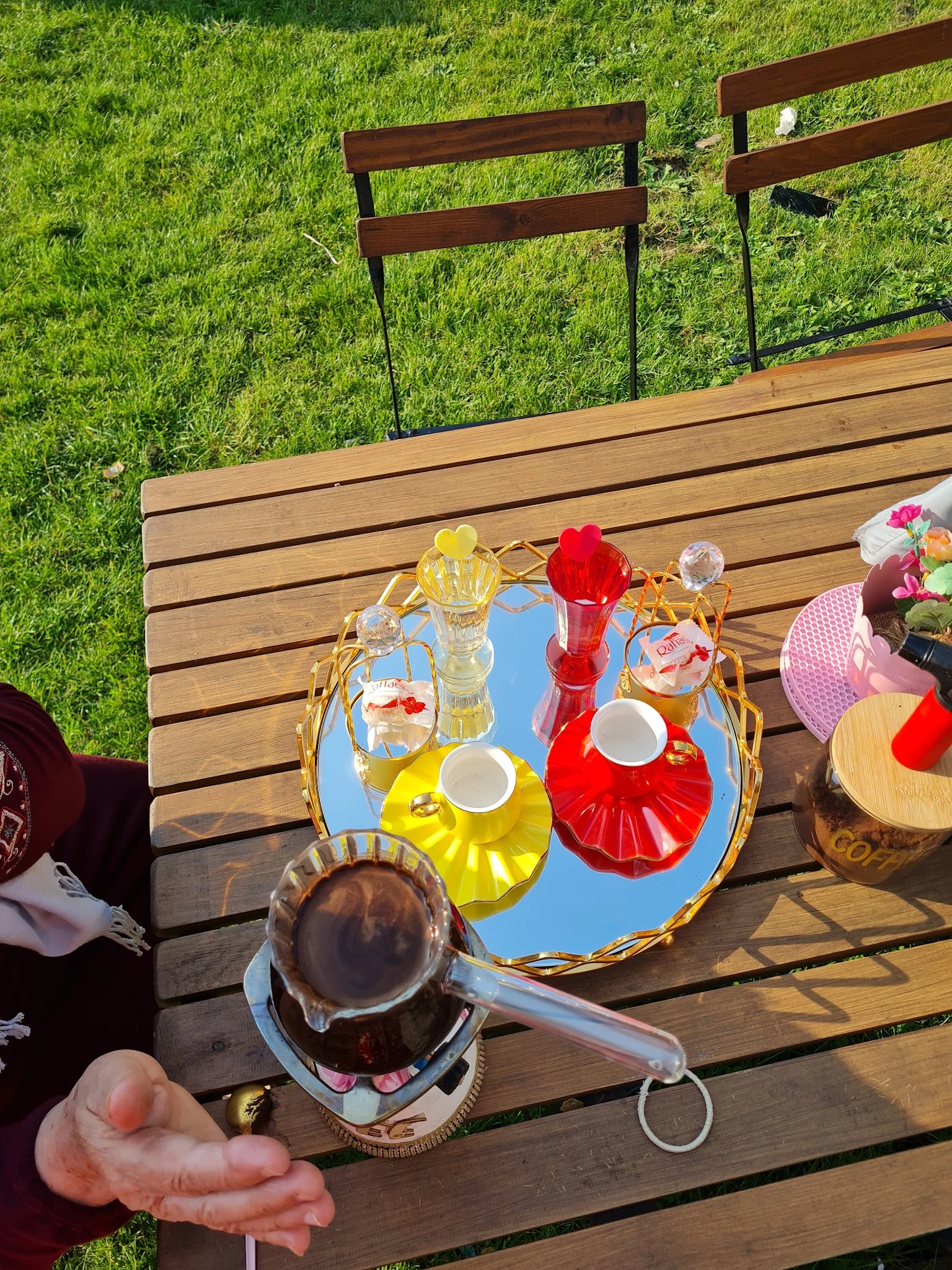 Terras met houten tafel, blauwe dienblad met glazen flessen in verschillende kleuren, kopjes en bloemen