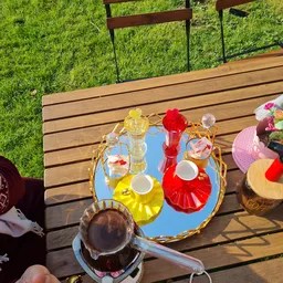 Terras met houten tafel, blauwe dienblad met glazen flessen in verschillende kleuren, kopjes en bloemen