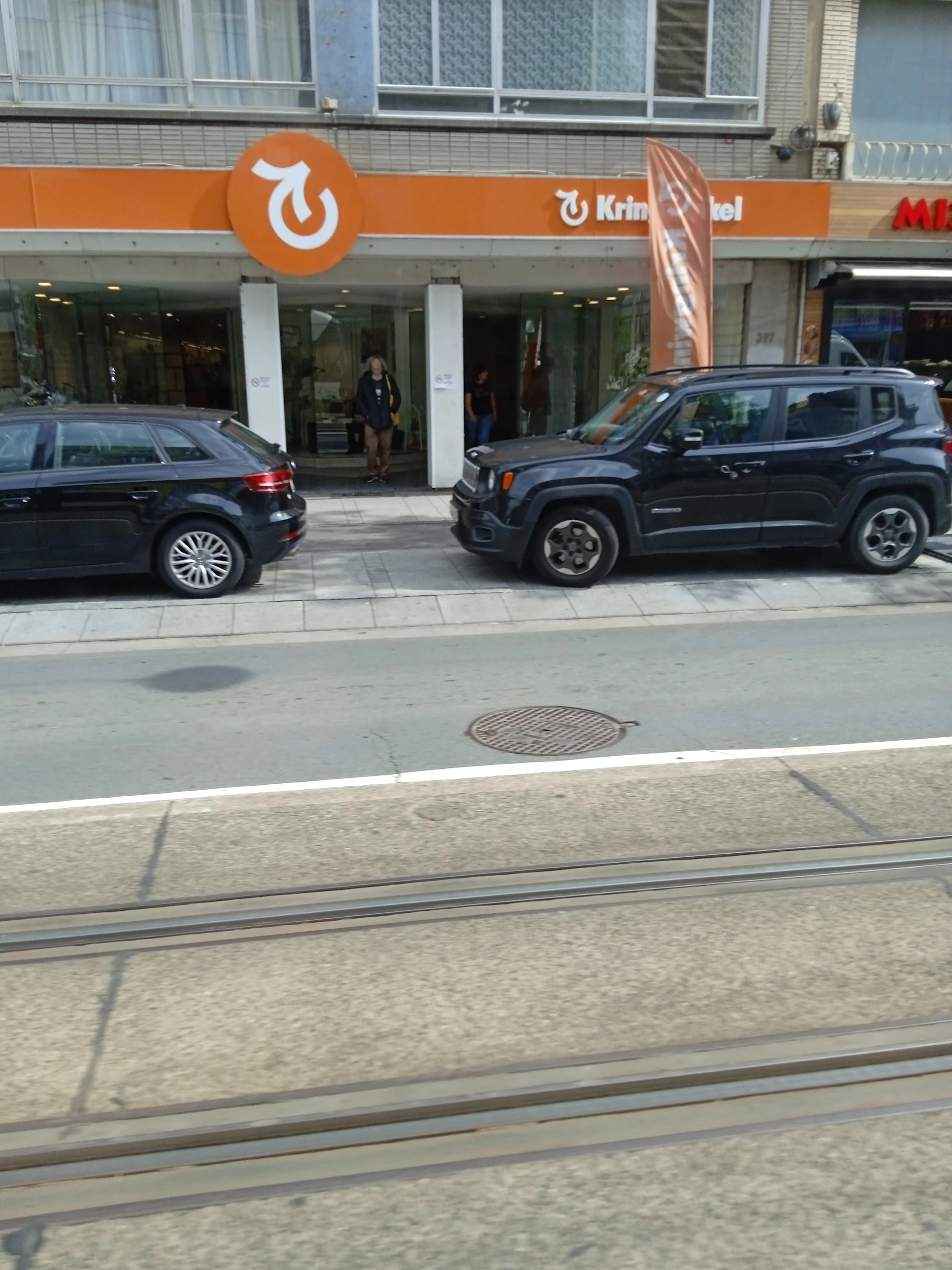 Straatvoorgevel met twee geparkeerde auto's en winkelentree met witte zuilen