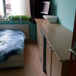 Tweedehands houten dressoir met blauwe bedsprei zichtbaar op achtergrond
