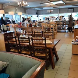 Ruim winkelbinnenruimte met houten meubels, stoelen en tafels, enkele bezoekers, moderne verlichting en grote ramen