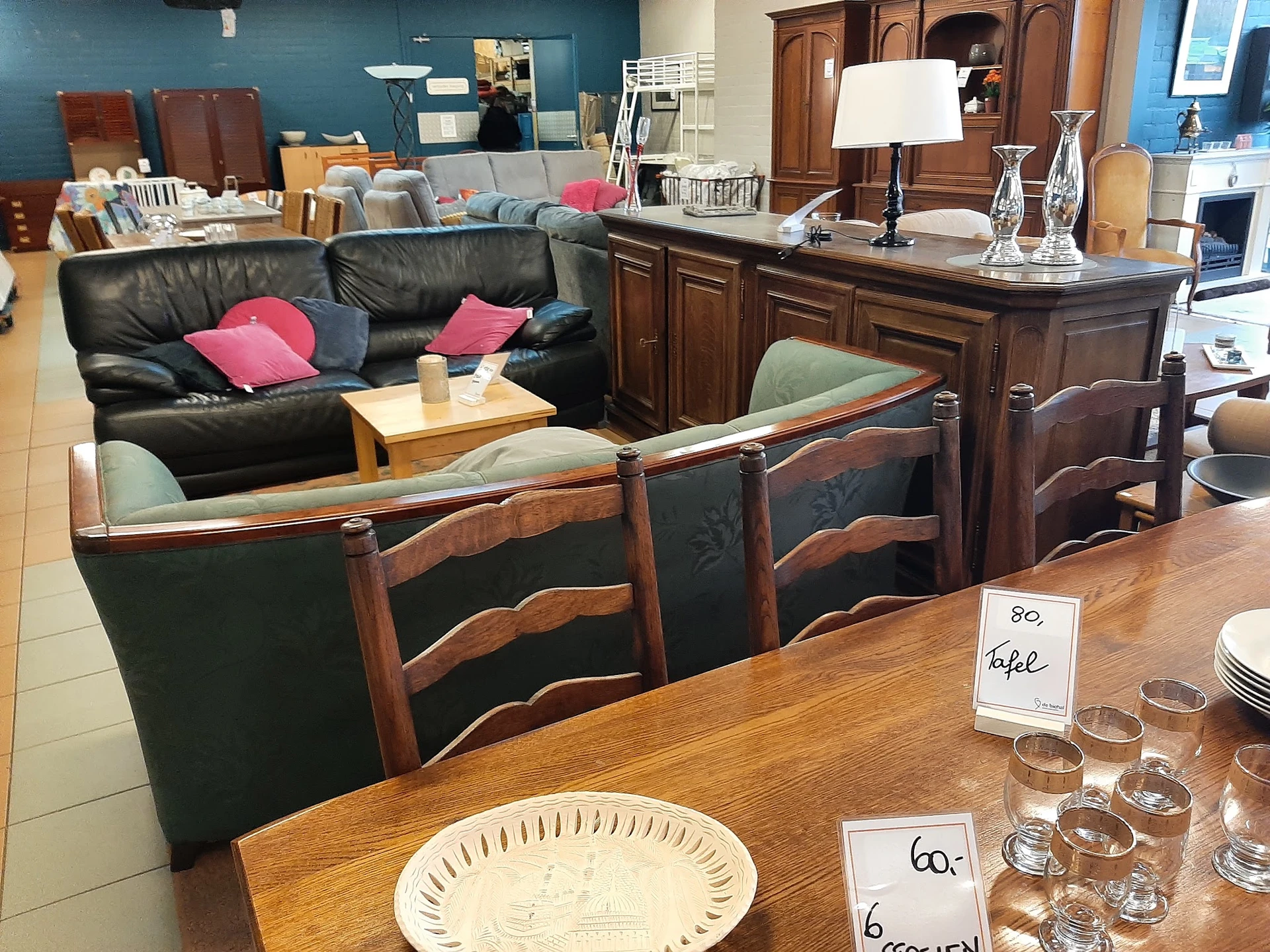 Winkelvloer met houten eettafel, stoelen, zwarte leren bank en houten meubelen in de achtergrond