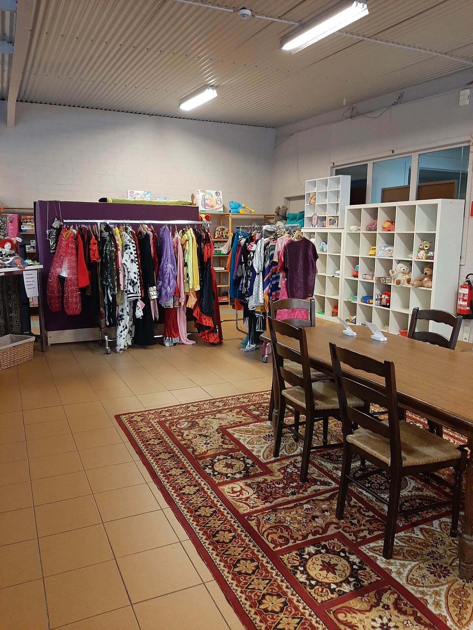 Winkelvloer met kledingrekken, witte stellingen met spullen en houten stoelen bij een tafel