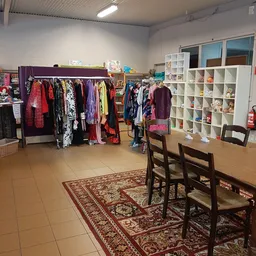 Winkelvloer met kledingrekken, witte stellingen met spullen en houten stoelen bij een tafel