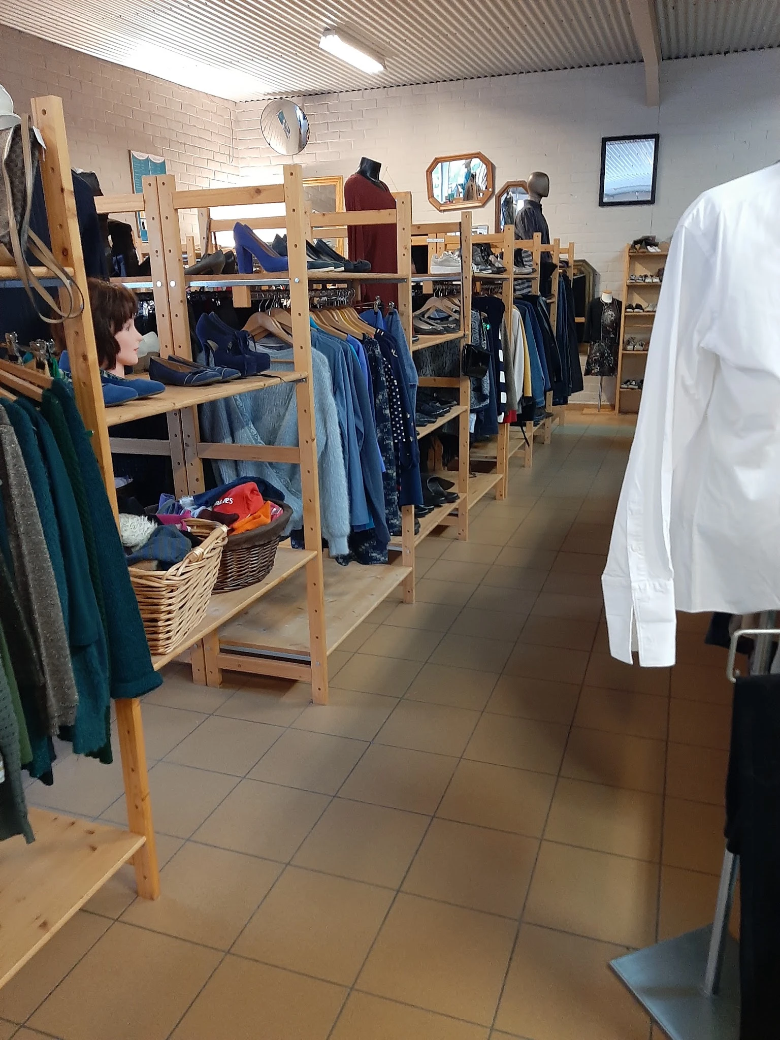 Winkelvloer met houten stellingen vol tweedehands kleding, daaronder mandjes met kleurig aanbod