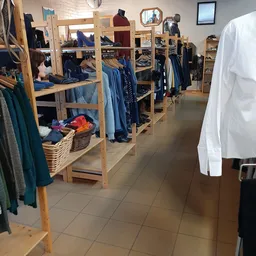 Winkelvloer met houten stellingen vol tweedehands kleding, daaronder mandjes met kleurig aanbod