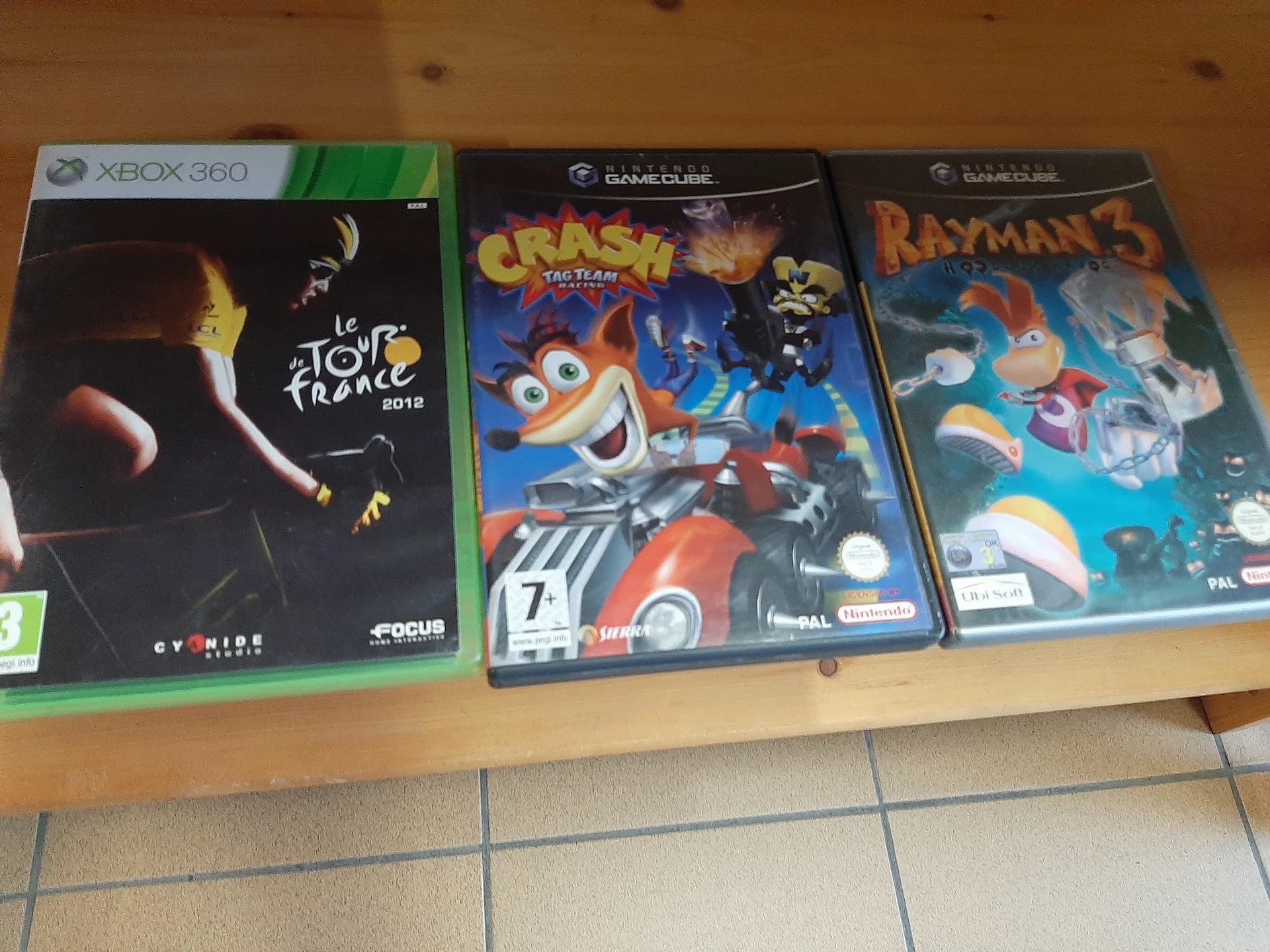 Drie tweedehands videogames op houten plank: Xbox 360 Tour de France, GameCube Crash Tag Team Racing en GameCube Rayman 2