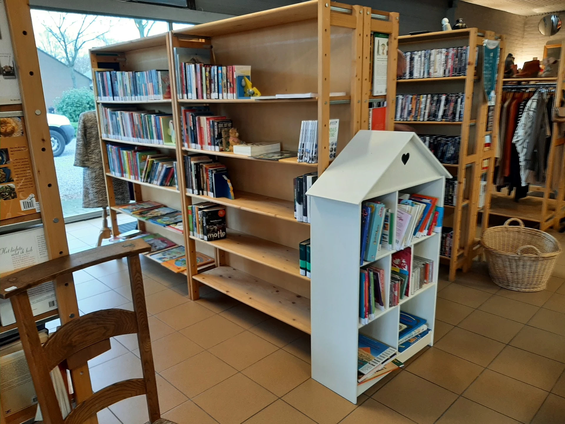 Winkelvloer met houten boekenkasten, een wit huisvormig boekenrek en hangrekken met kleding