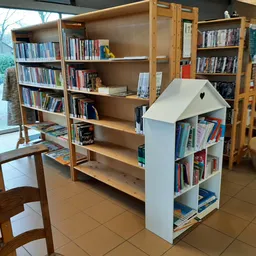 Winkelvloer met houten boekenkasten, een wit huisvormig boekenrek en hangrekken met kleding