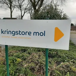 Wit bord met logo en naam van kringloopwinkel aan ingang, groen onderhoud eronder