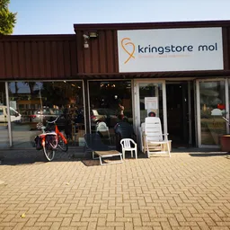Gevel van kringloopwinkel Mol met bruine containerbouw, grote ramen, ingang en uitstallingen op het terras
