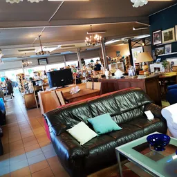 Winkelinterieur met zwarte leren bank met gekleurde kussens, tv, houten meubels en stellingen met diverse spullen op de achte