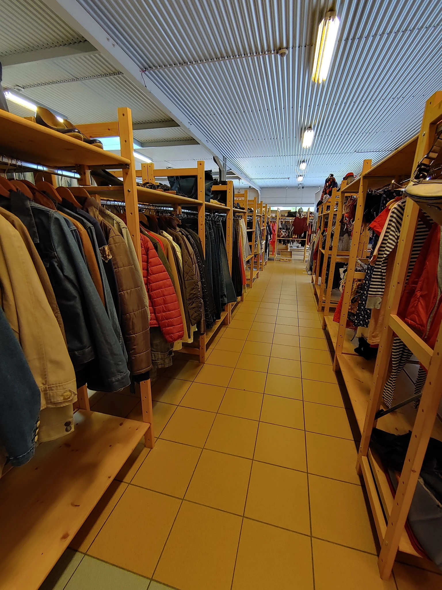 Winkelgang met houten kledingrekken aan beide zijden, vol met tweedehands jassen en kleding in verschillende kleuren