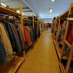 Winkelgang met houten kledingrekken aan beide zijden, vol met tweedehands jassen en kleding in verschillende kleuren