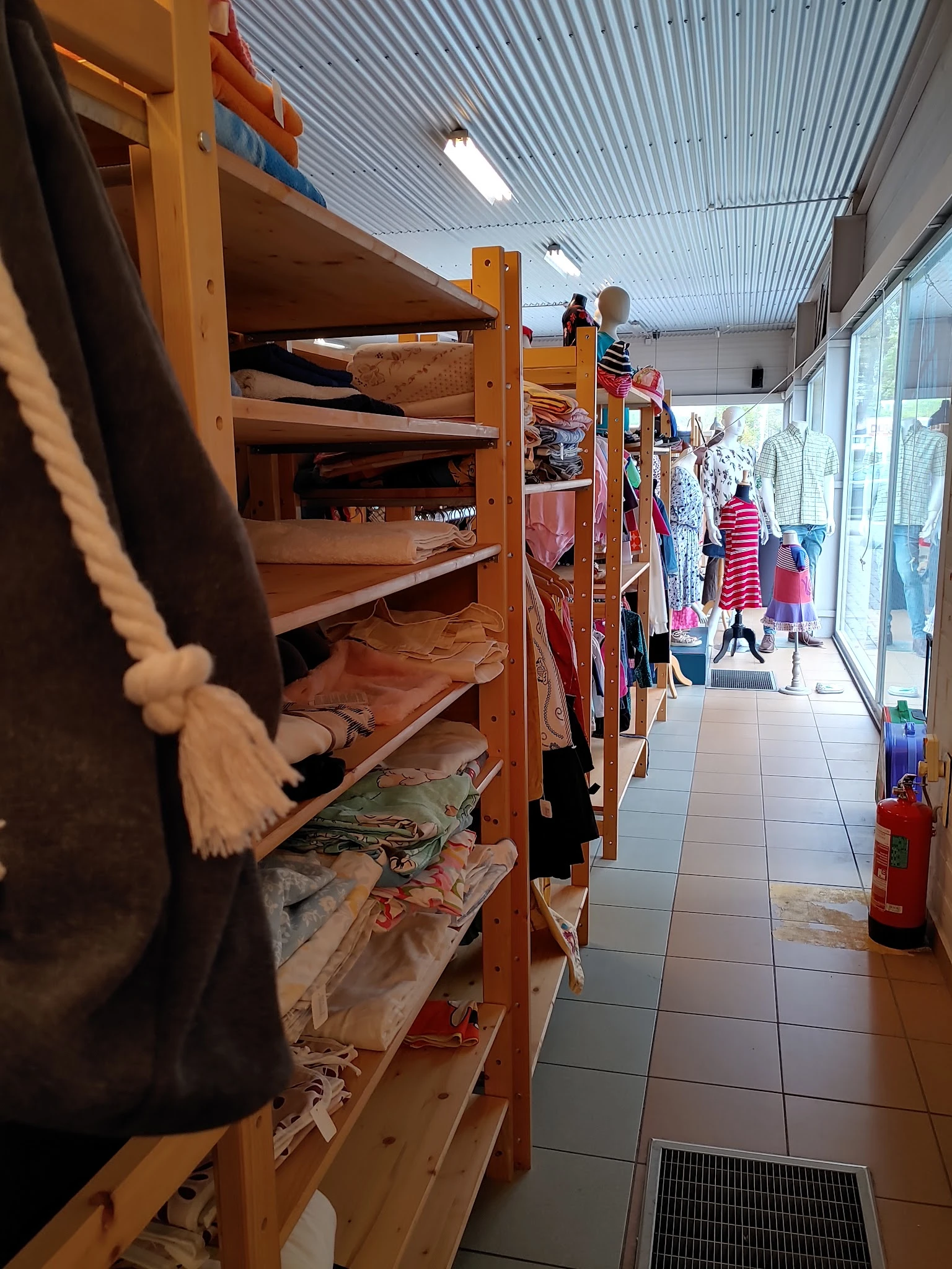 Smalle winkelgang met houten stellingen vol tweedehands kleding en mannequins langs de wanden