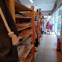 Smalle winkelgang met houten stellingen vol tweedehands kleding en mannequins langs de wanden