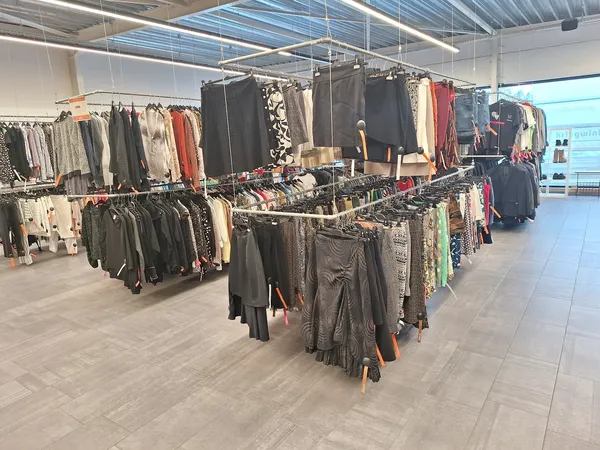 Winkelvloer met meerdere kledingrekken vol tweedehands kleding, onder een verlichte plafondstructuur