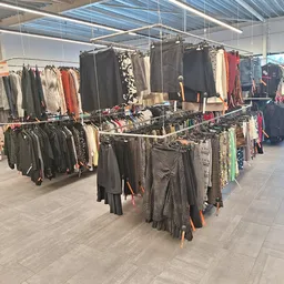 Winkelvloer met meerdere kledingrekken vol tweedehands kleding, onder een verlichte plafondstructuur