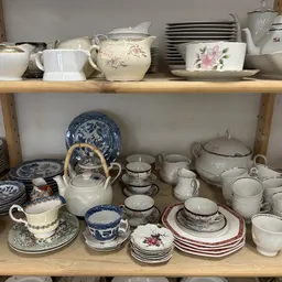 Twee houten schappen vol met serviesgoed, kopjes, schotels, kannen en decoratieve porseleinen items in crème en blauw