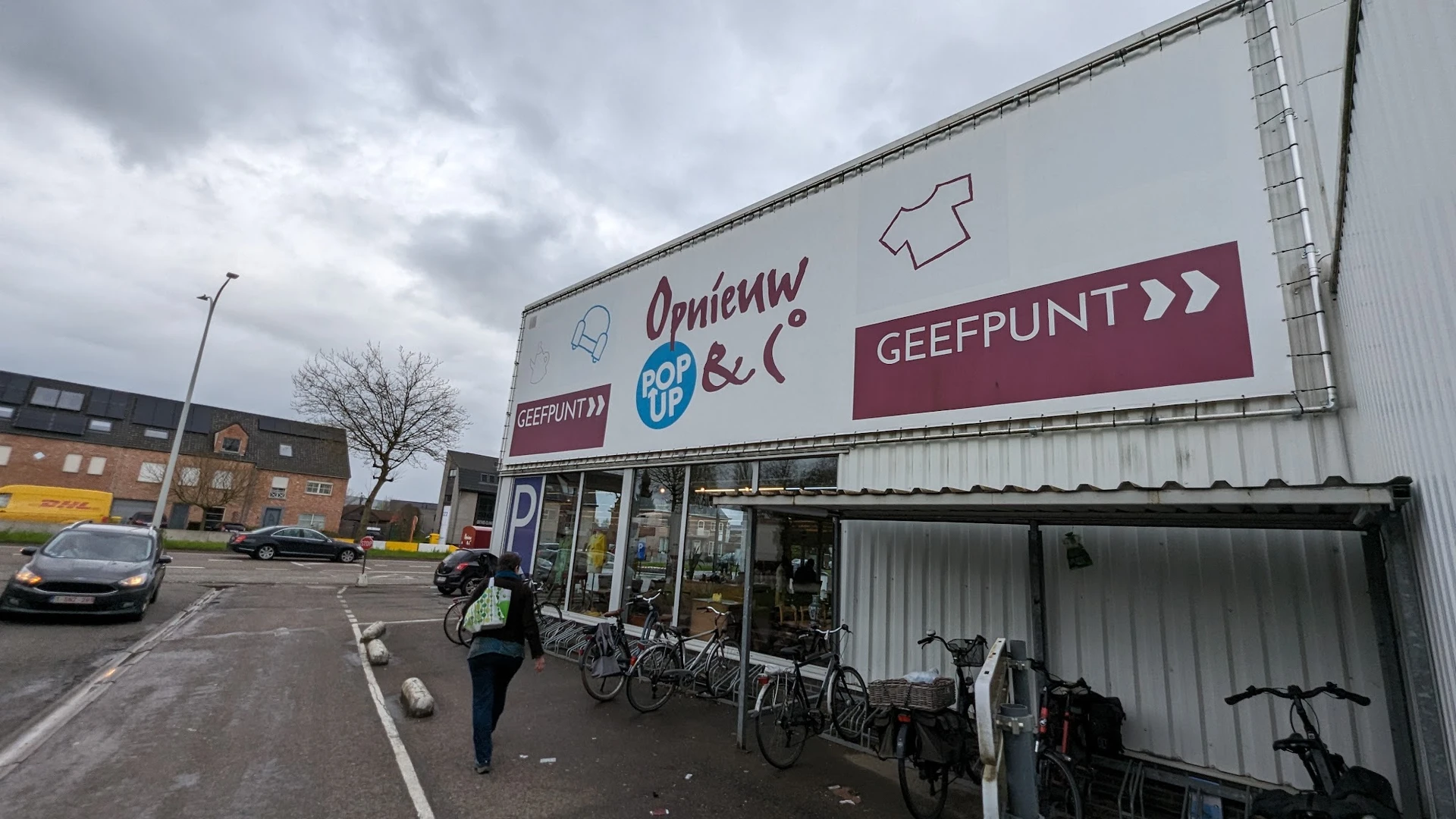 Voorgevel van kringloopwinkel met grote uithangborden en fietsen geparkeerd ervoor