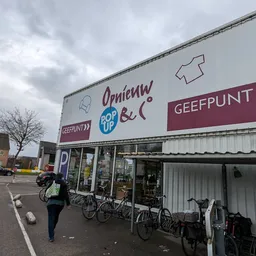 Voorgevel van kringloopwinkel met grote uithangborden en fietsen geparkeerd ervoor