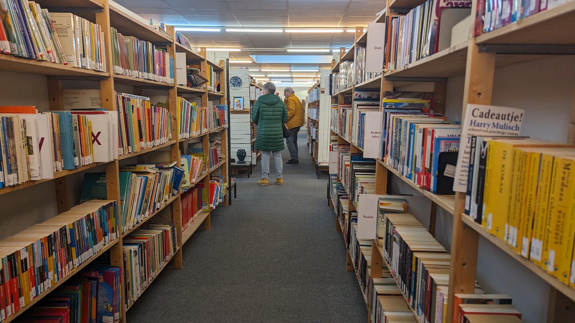 Boekenrekken langs een gang in de winkel met bezoekers die tussen de stellingen lopen