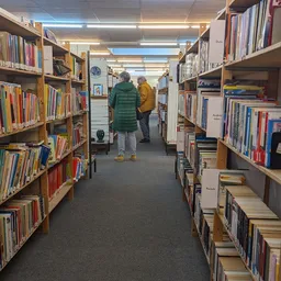 Boekenrekken langs een gang in de winkel met bezoekers die tussen de stellingen lopen