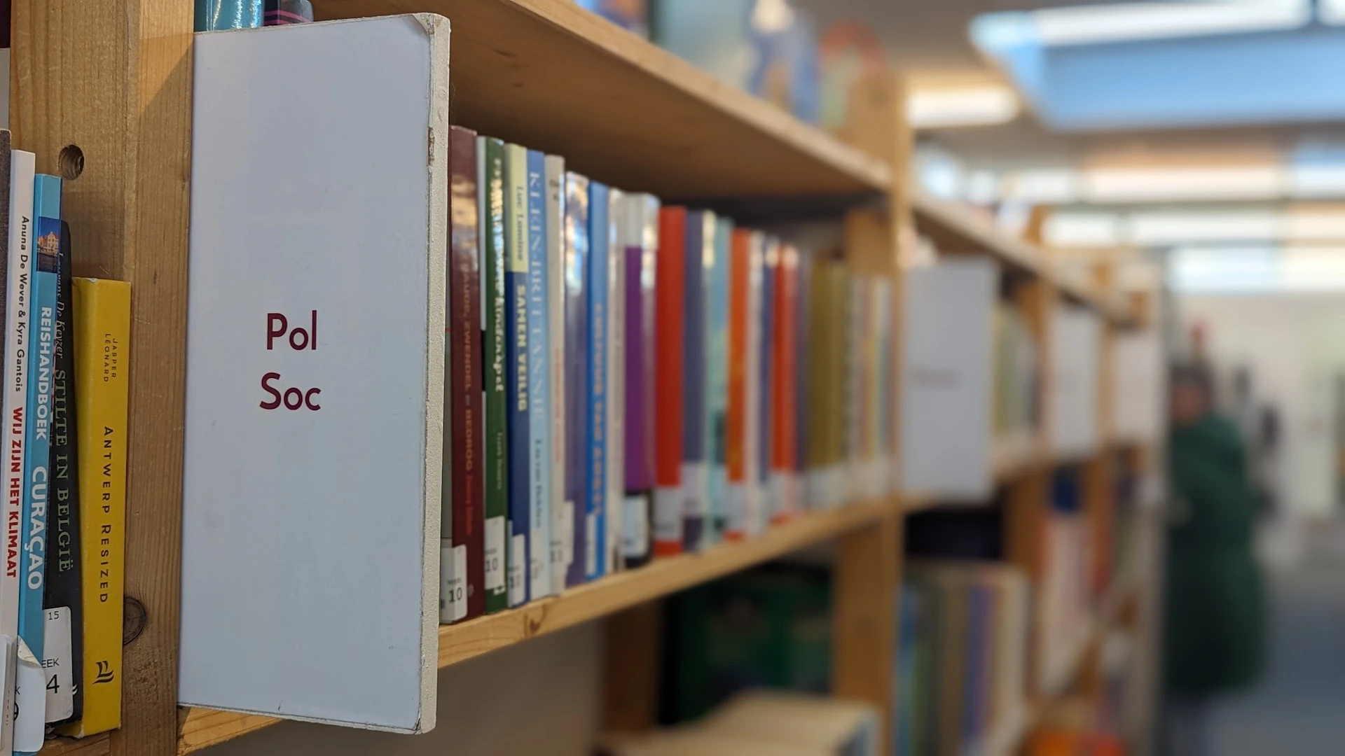 Boekenrek met label 'Pol Soc' en diverse boeken met gekleurde ruggen in een kringloopwinkel