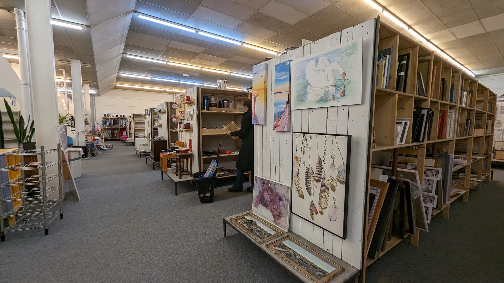 Winkelvloer met stellingen, boekenrekken, kunstwerken op wit bord en diverse tweedehandsartikelen
