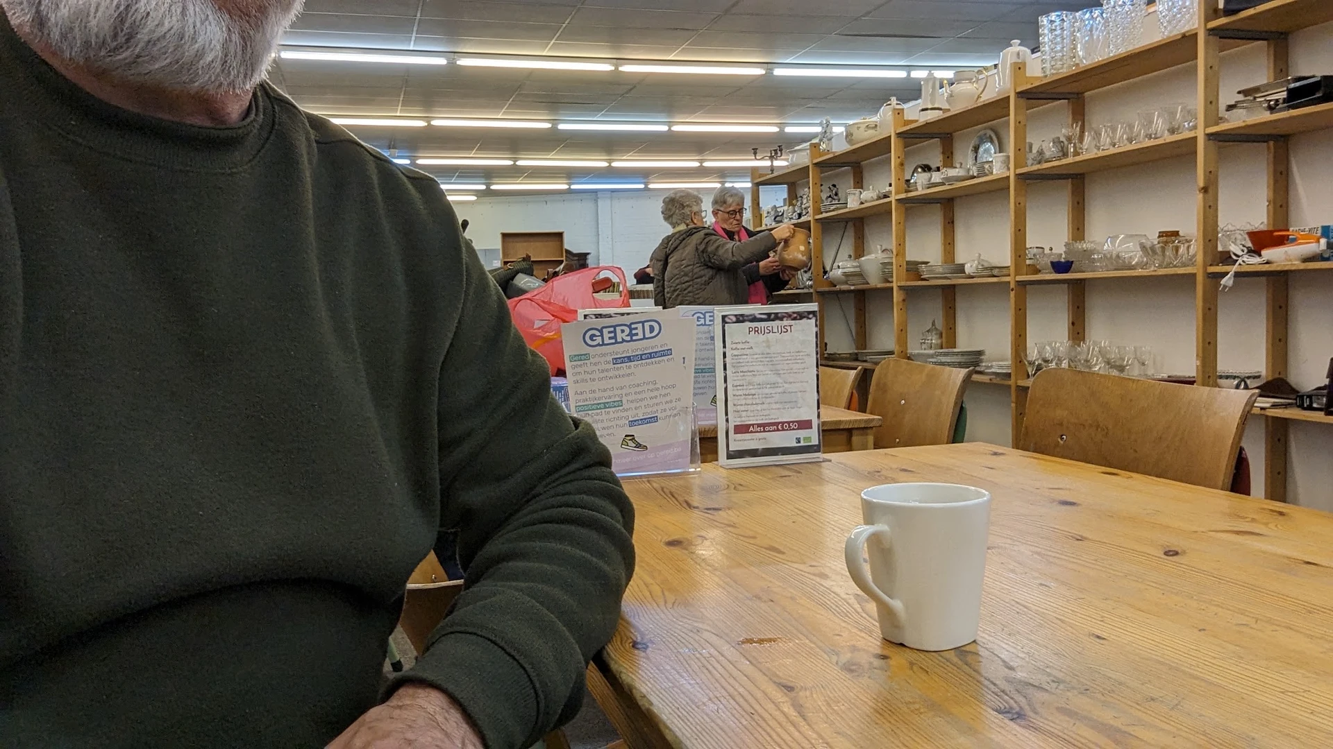 Persoon aan houten tafel met koffiemok in lunchhoek van kringloopwinkel