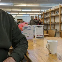 Persoon aan houten tafel met koffiemok in lunchhoek van kringloopwinkel