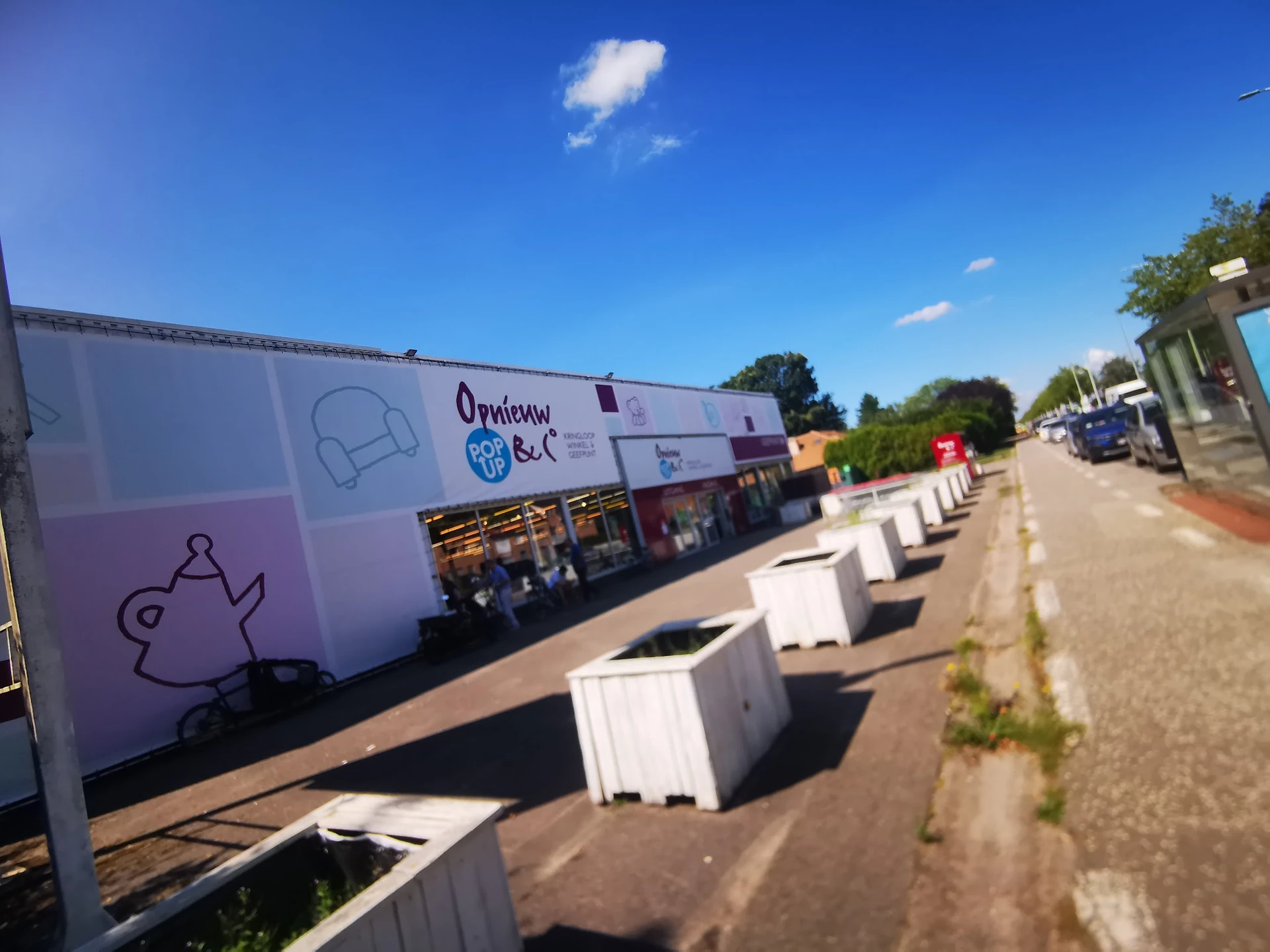Voorgevel van kringloopwinkel Opnieuw & Co aan de straat met witte plantenbakken ervoor
