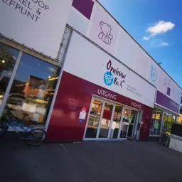 Gevel van kringloopwinkel met witte en bordeauxrode bekeding, winkelnaam Opnieuw & Co zichtbaar, grote etalageruiten en ingan