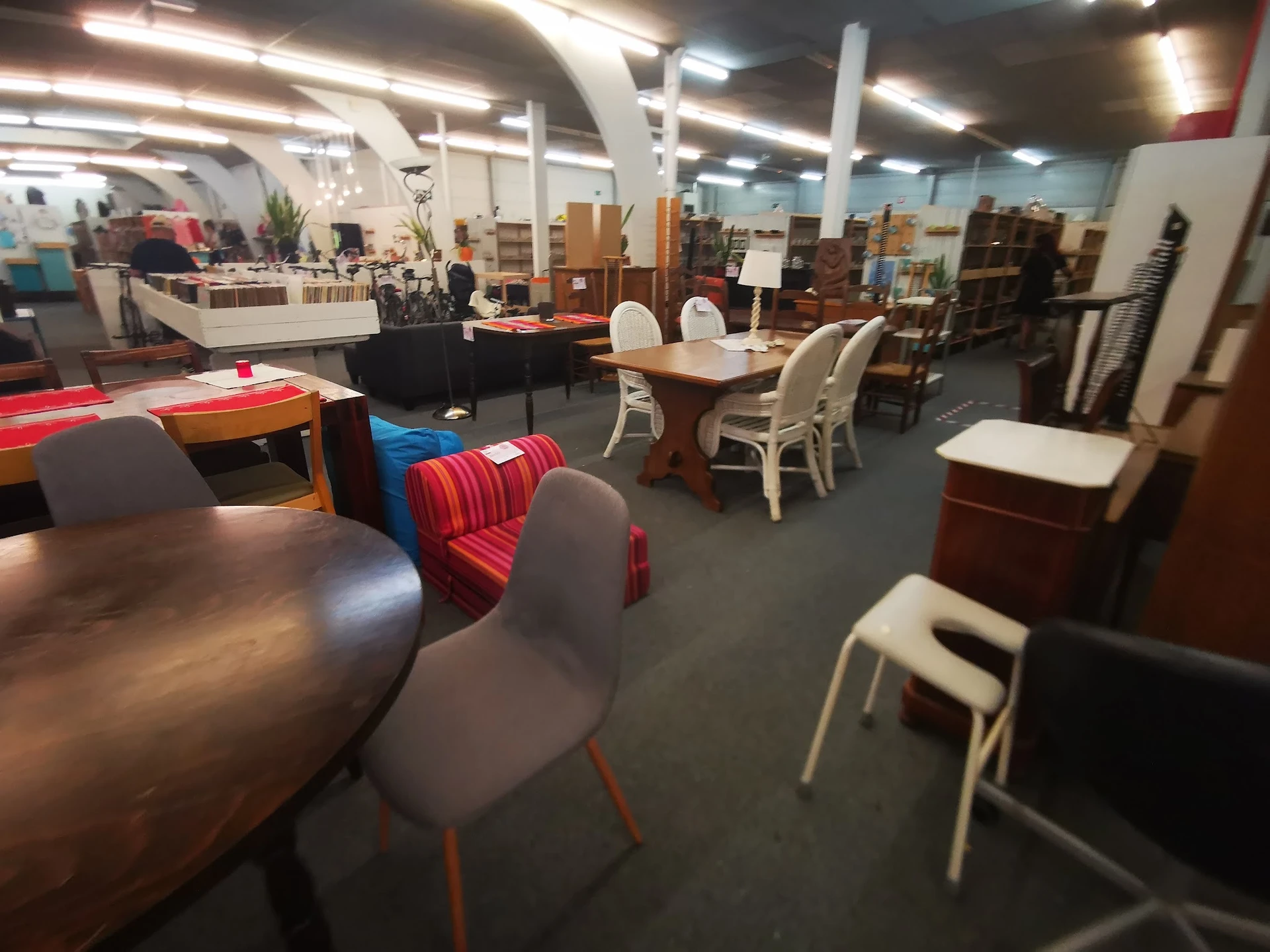 Winkelvloer met diverse meubels: tafels, stoelen, kasten en decorstukken uitgestald op grijze vloer onder fluorescente verlic