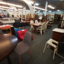 Winkelvloer met diverse meubels: tafels, stoelen, kasten en decorstukken uitgestald op grijze vloer onder fluorescente verlic