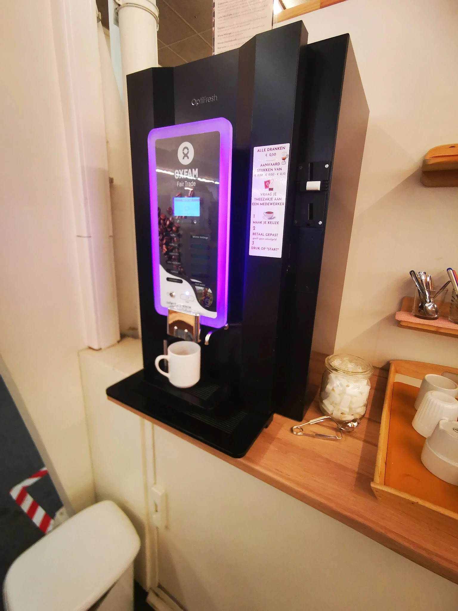 Zwarte koffiemachine met paarse verlichting en witte mok op een zwart blad