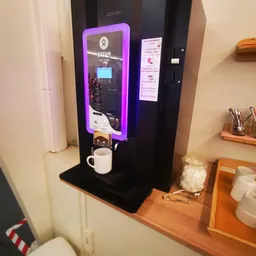 Zwarte koffiemachine met paarse verlichting en witte mok op een zwart blad