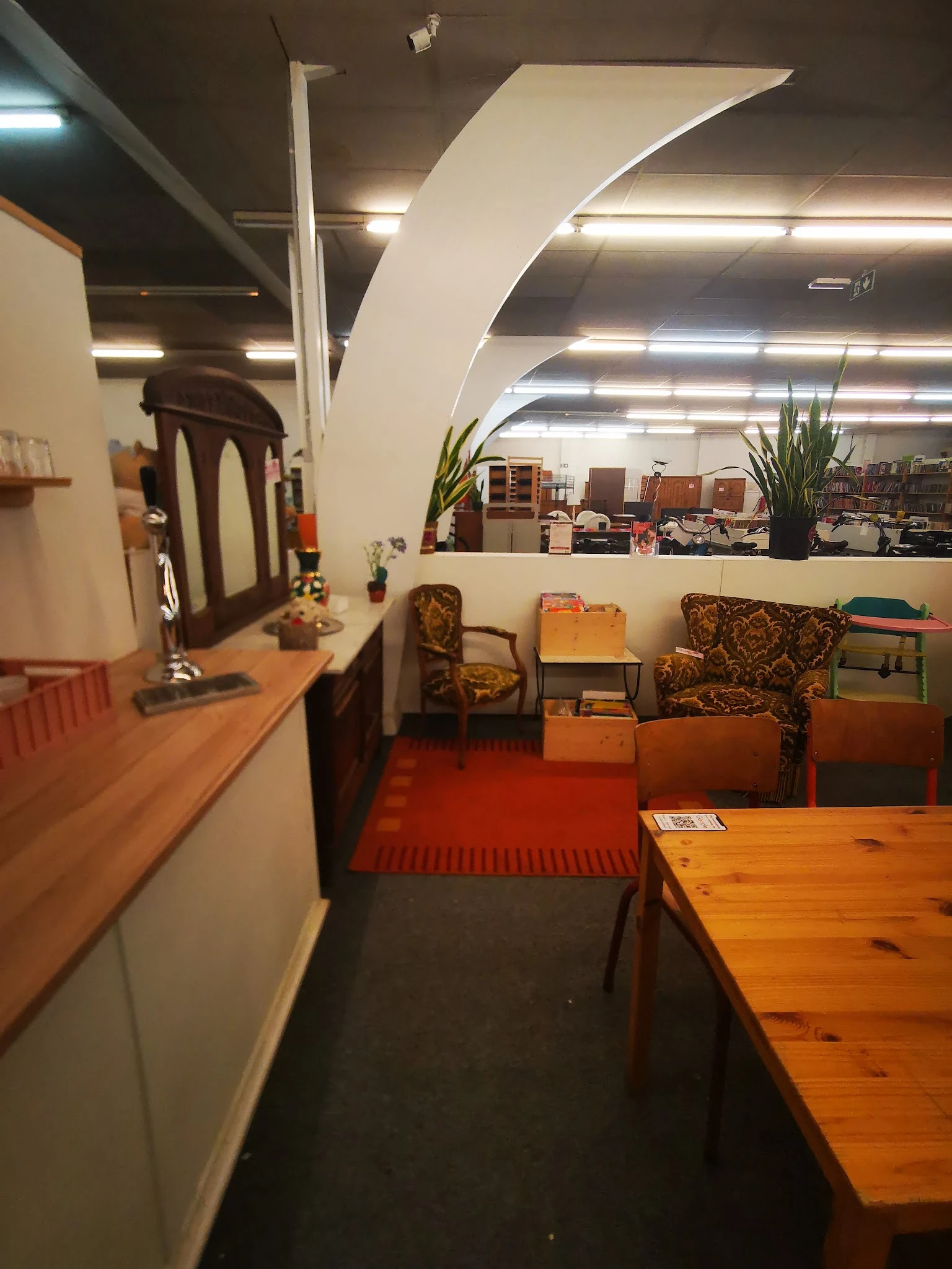 Winkelinterieur met houten meubels, fauteuils en diverse huishoudartikelen langs rode vloerbedekking